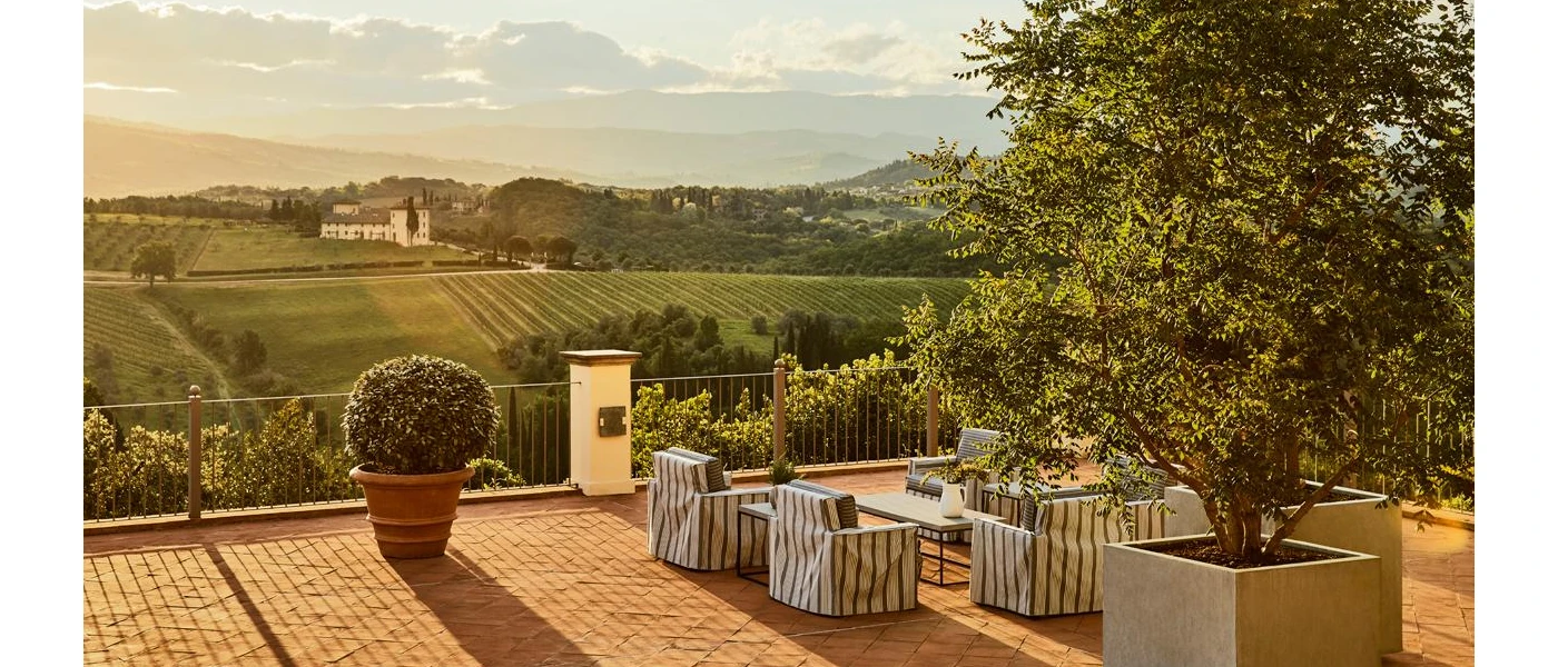 Outdoor terrace with striped armchair-style seating, terracotta-potted plants, and a view of the Tuscan countryside