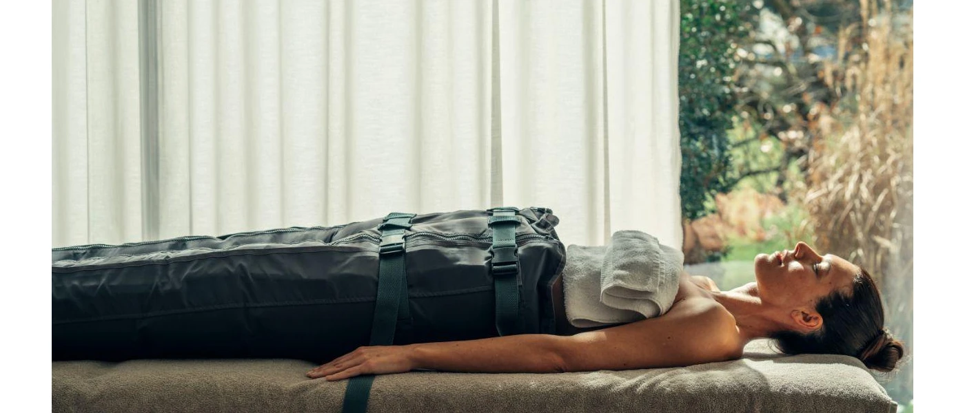 Female lies with her eyes closed on a massage bed in a sleeping bag-style cover