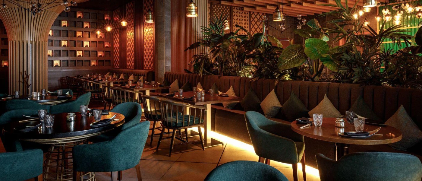 Glamorous restaurant with glossy plants, brown sofa-like seating and blue chairs, dark-wood tables and lantern-like lights