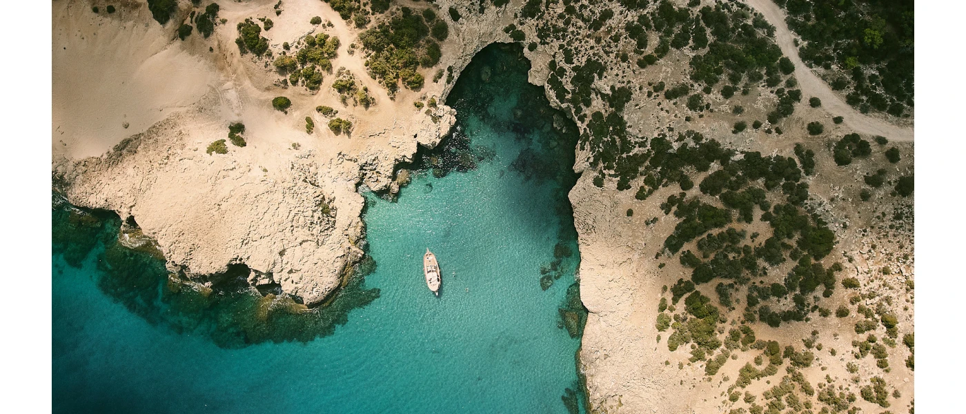 Aerial view of a turquoise cove with a boat, surrounded by cliffs dotted with trees