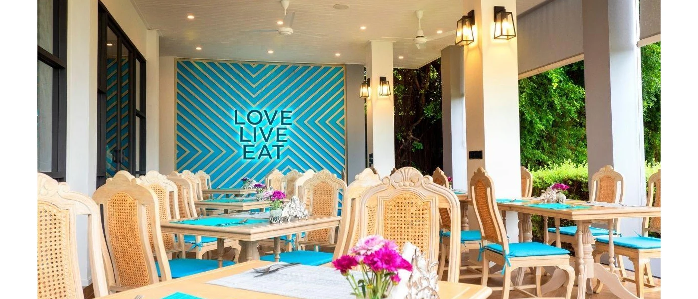 Light-wood tables and chairs with a blue statement wall that reads 'LOVE LIVE EAT'