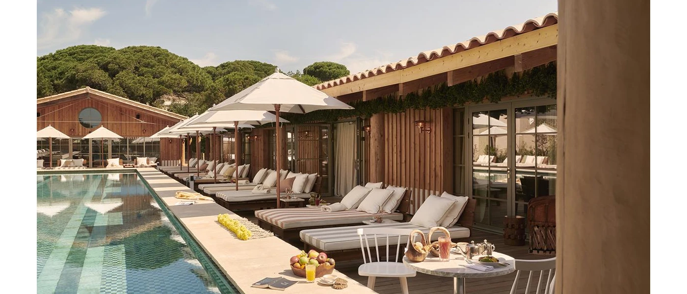 Swimming pool lined with chic striped-cushioned loungers, white umbrellas, and bowls of fruit and pastries