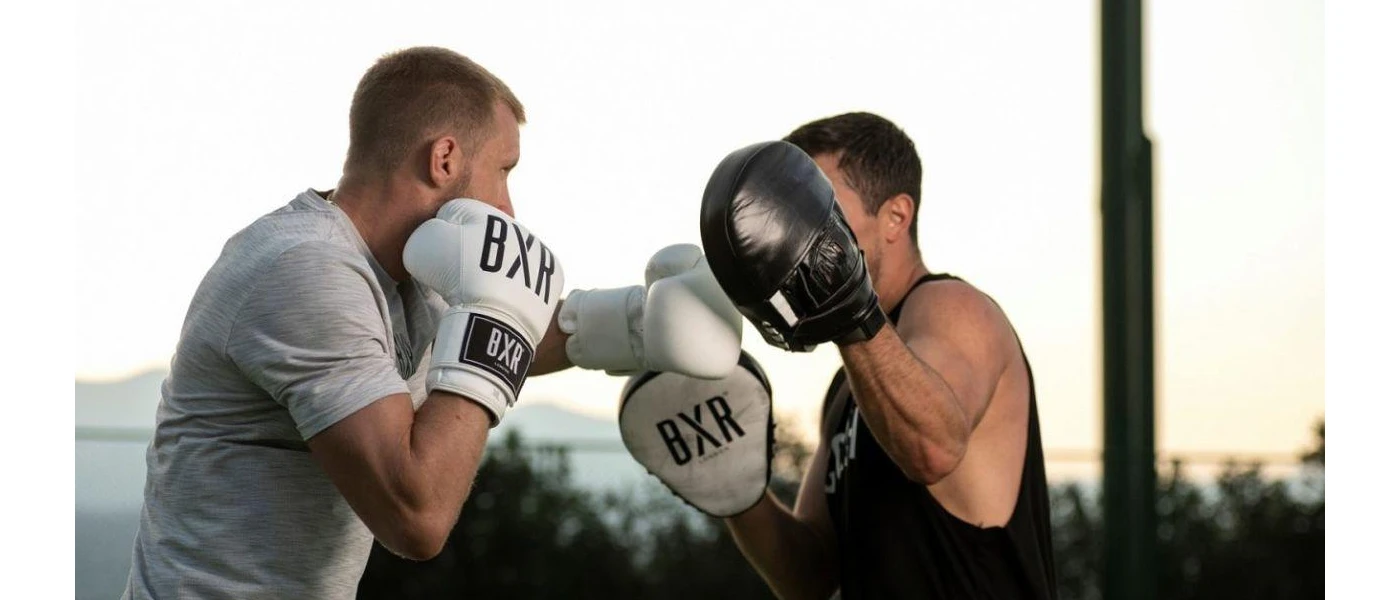 Two men in active wear box outdoors with mountains in the background