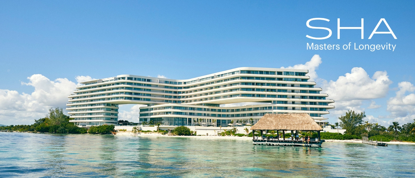 High-rise, multi-storey white resort on a white-sand beach overlooking the sea, under a blue sky with white clouds