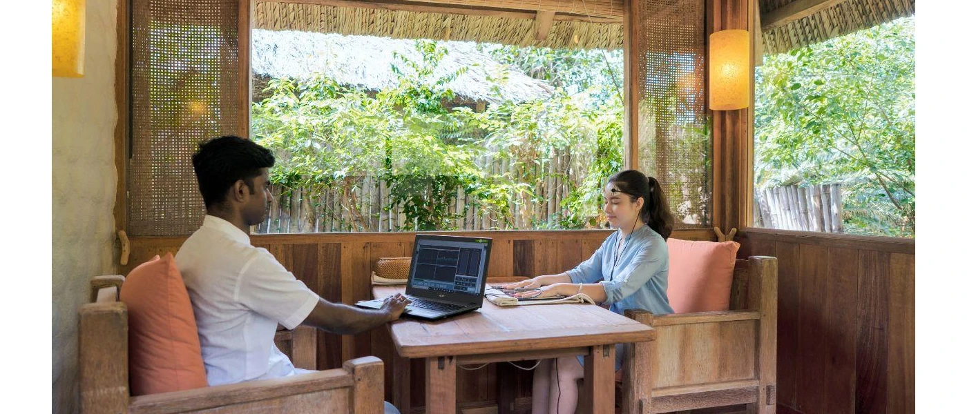 Woman sits with eyes closed in head gear as a professional assesses her results on a laptop screen across the desk