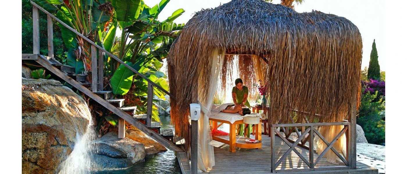 Woman lies on a bed in a thatched-roof open-sided cabana enjoying a massage in the tropical outdoors