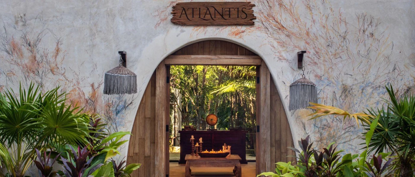 Stone-walled entrance to the Atlantis Spa, with an arched entrance fringed by greenery peering through to a wooden table covered in candles
