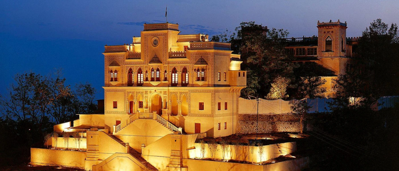 A colonial Indian palace lit up after dark, surrounded by greenery