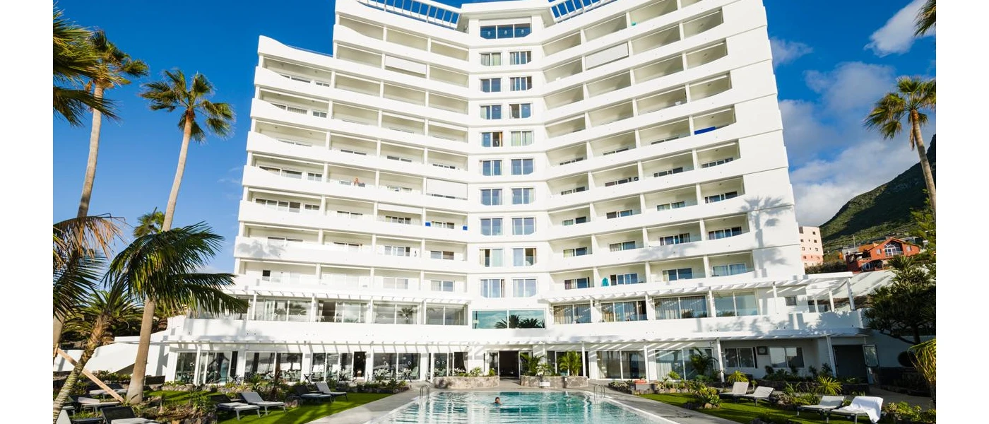 High-rise white hotel, swimming pool and palm trees under a blue sky