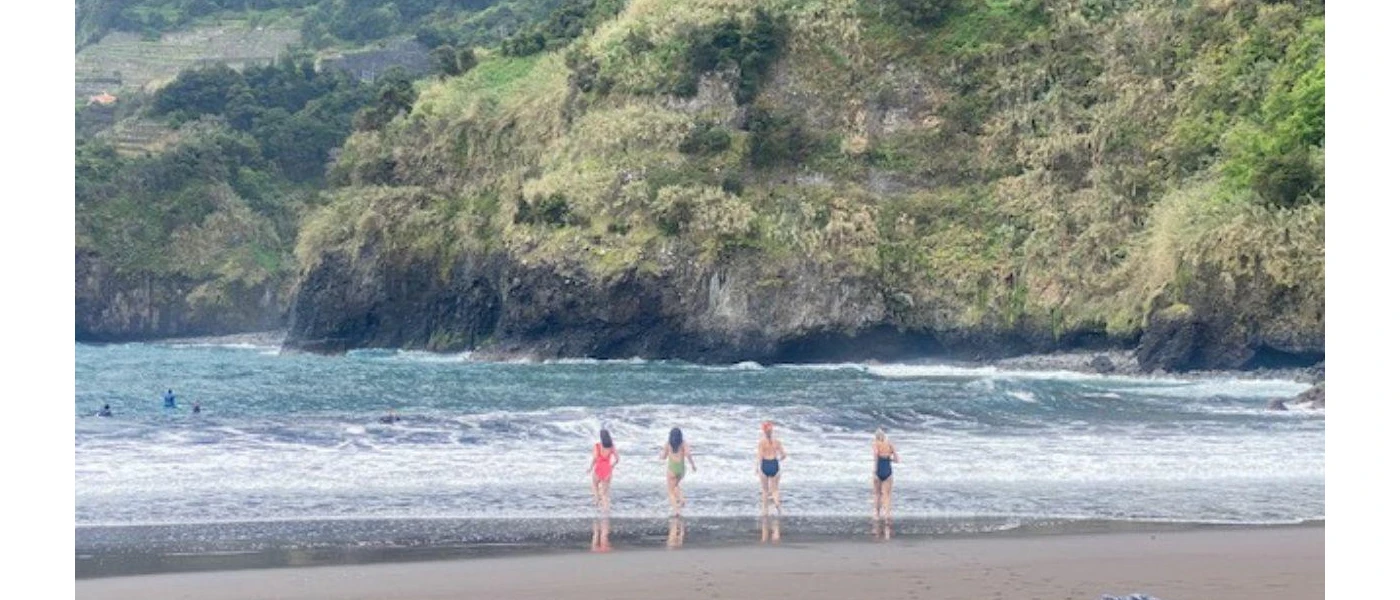 Four people in swimwear entering the sea with green mountains surrounding them