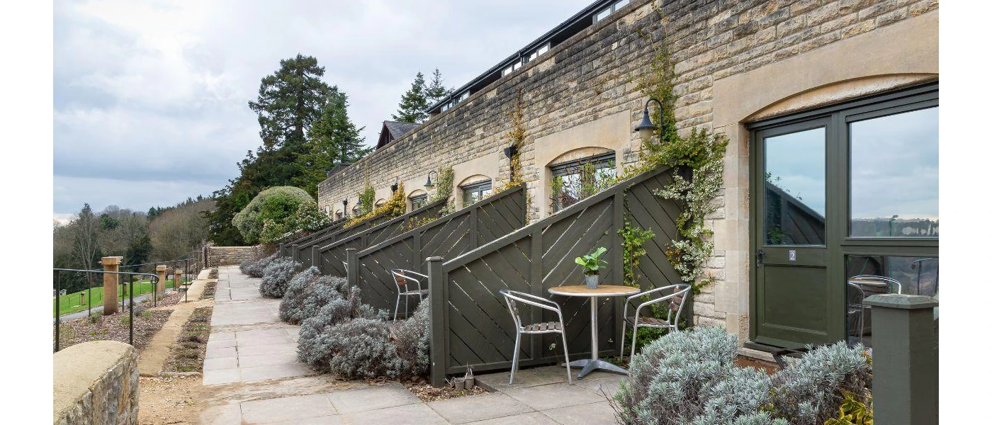Line of black double doors and paved patios furnished with table and chairs and shrubs