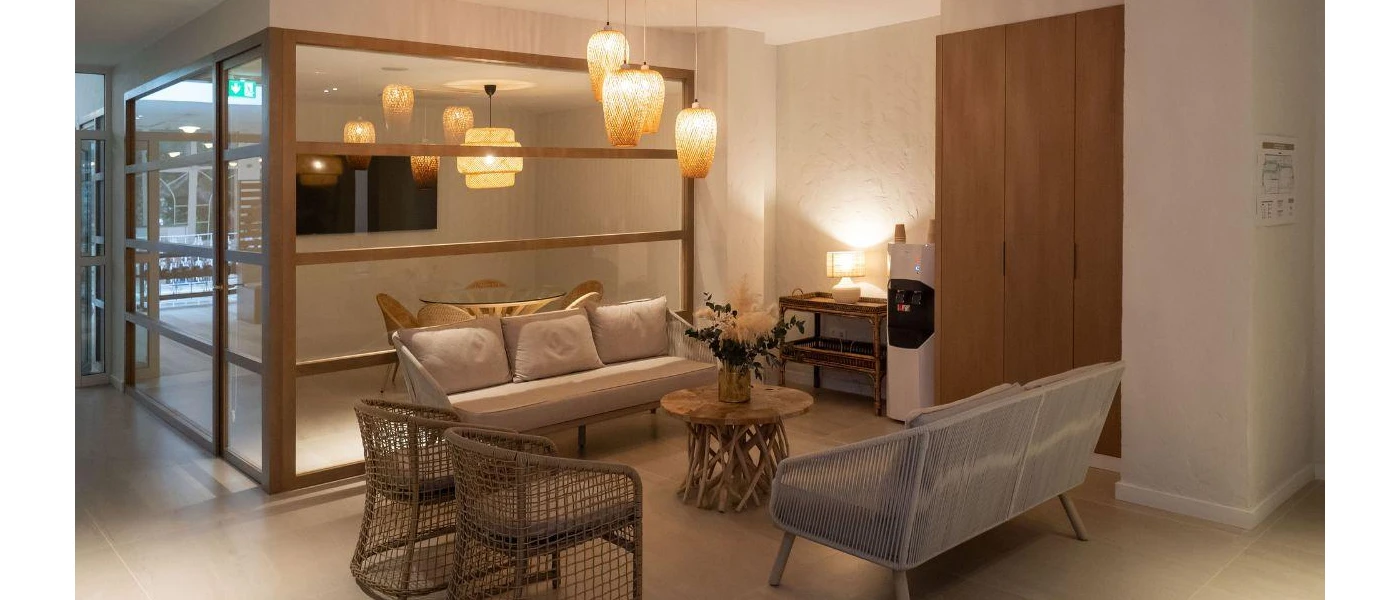 Cosy seating area with wooden partitions, stone-coloured cushions, a wooden coffee table made with driftwood and hanging rattan lantern-style lights