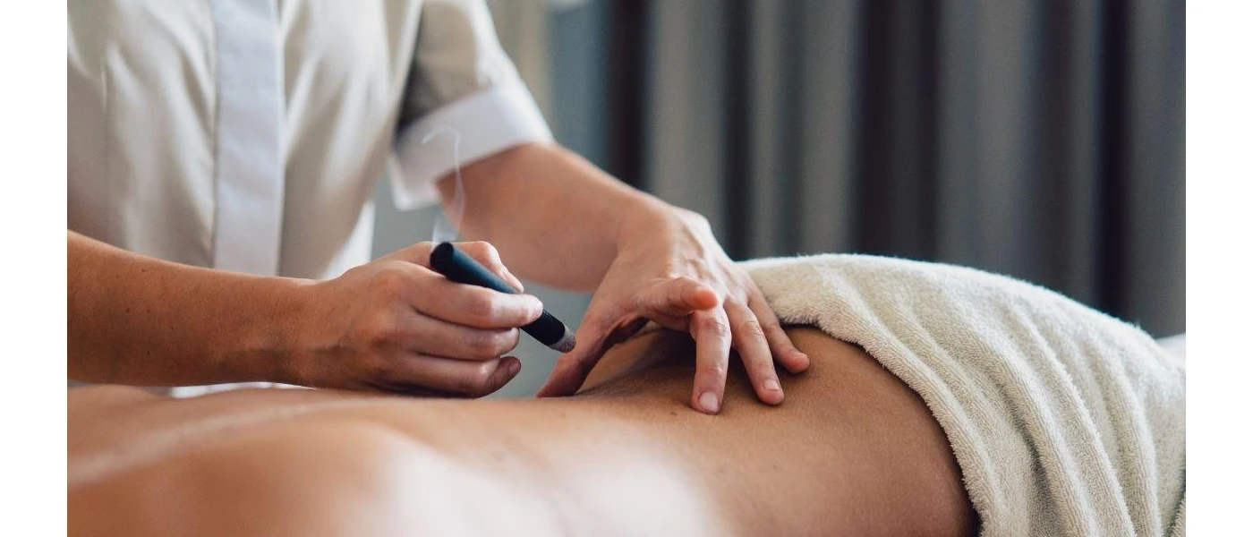 Guest lies on their front as a therapist holds a thick stick with smoke coming out of it over their back