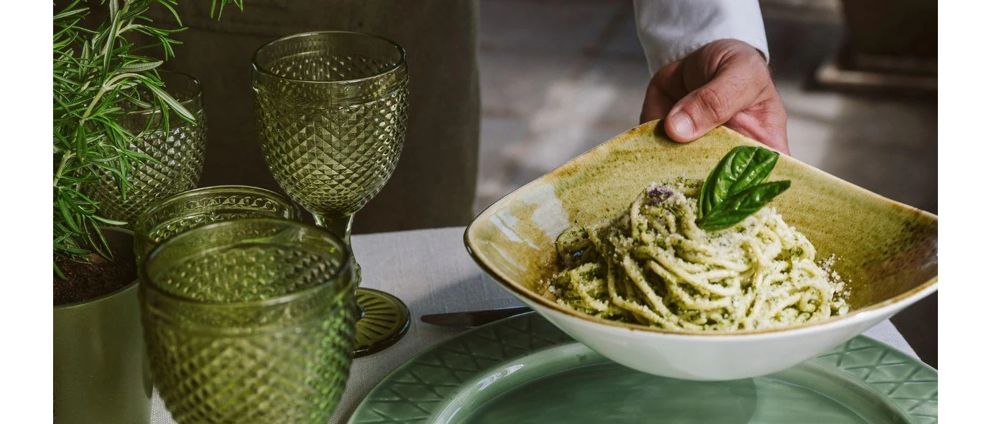 A chef holding a plate of creamy spaghetti, topped with basil leaves