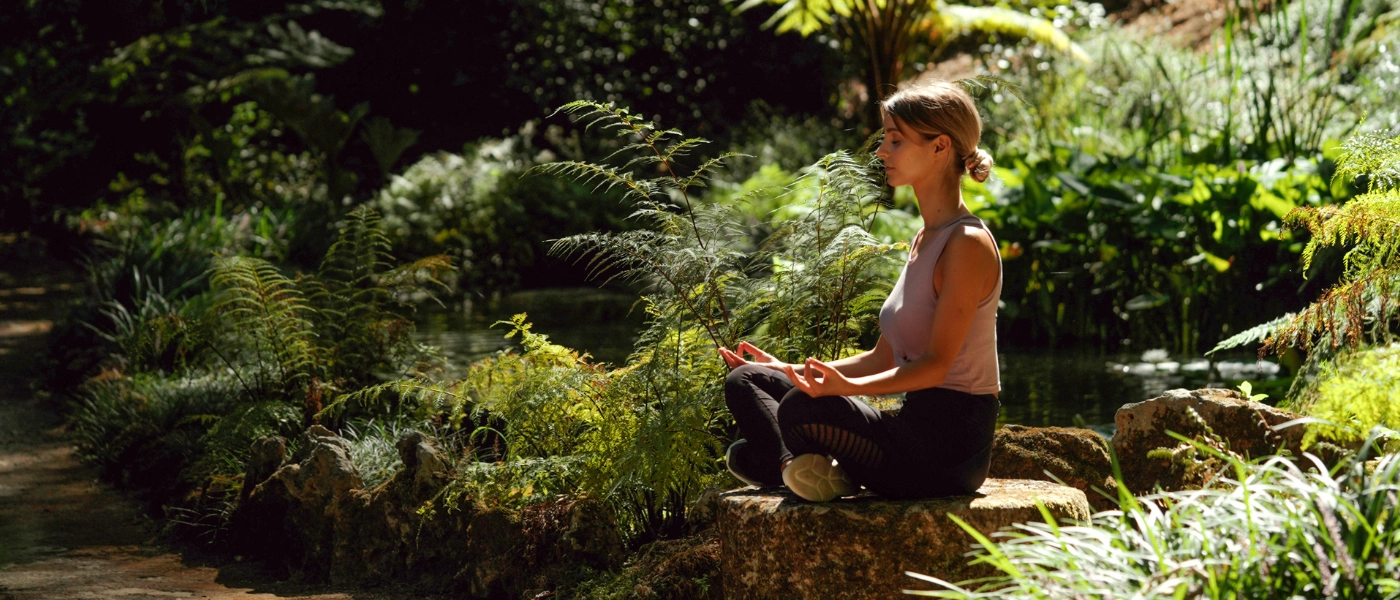 Woman in black leggings and white top sitting on a rock meditating 