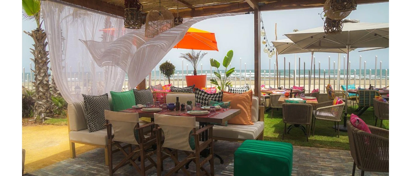 Open-sided seating area with green soft furnishings and white curtained sides blowing in the wind