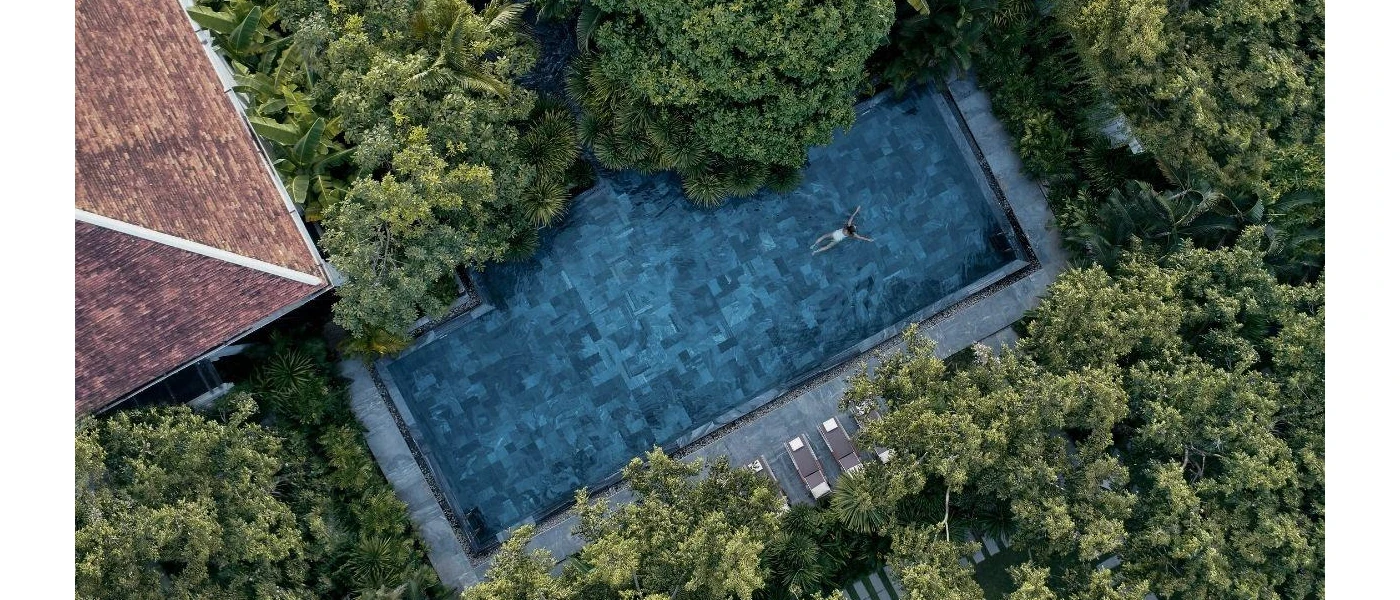 Woman in a white swimsuit in a pool surrounded by tropical greenery, as seen from the air
