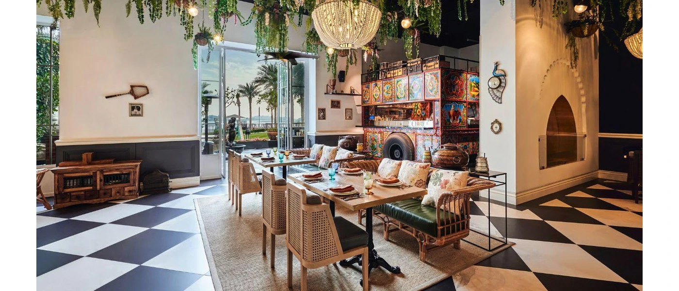 Restaurant interior with black and white chequered flooring, a glittering chandelier, hanging plants, rattan chairs and a colourful bus design