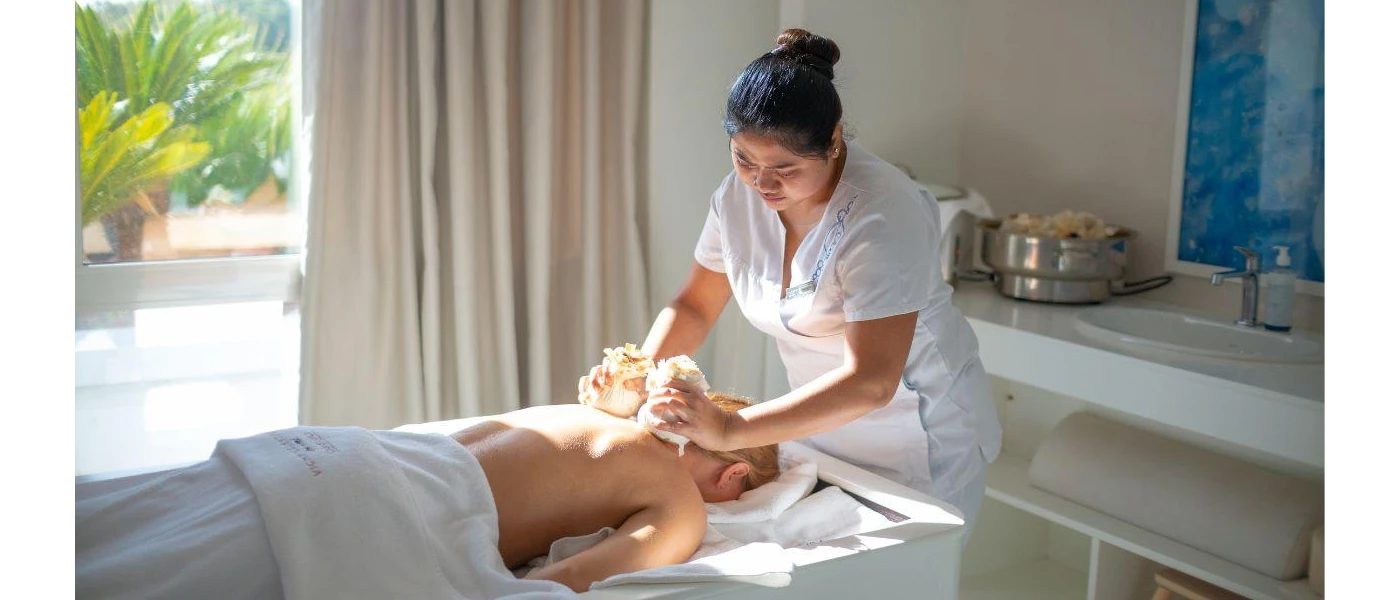 Woman with dark hair in white uniform massage a person lying on a bed with a white towel over them