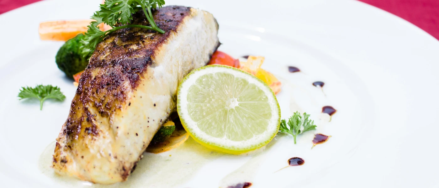 Fillet of grilled fish plated up with a slice of lemon and a herb garnish