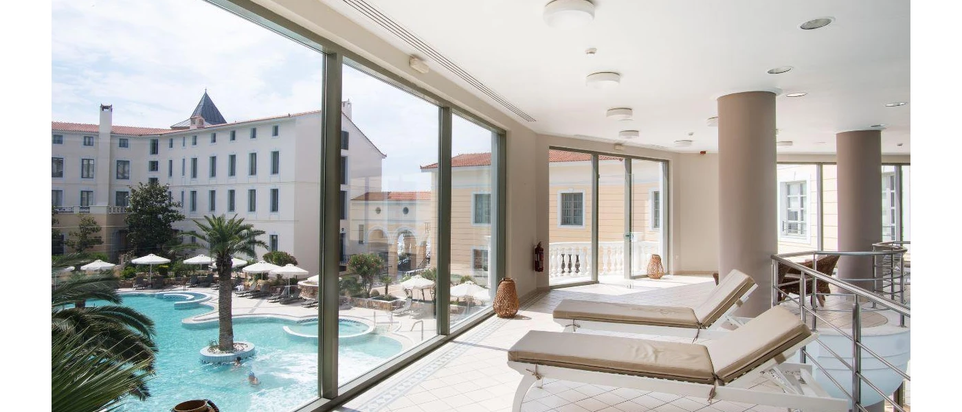 Indoor spa area with cream loungers and floor-to-ceiling windows overlooking a swimming pool