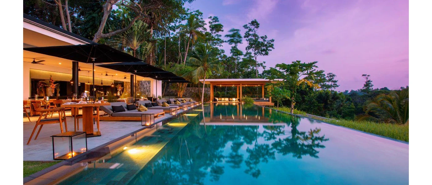 Infinity pool lined with lit lanterns and surrounded by blue cushioned loungers and jungle greenery
