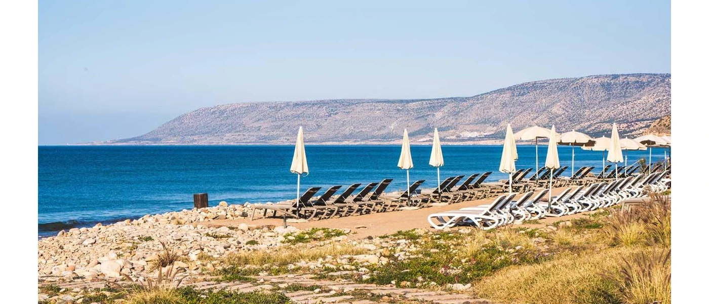 Sandy beach with loungers, white umbrellas and the ocean and mountains in the foregrounf