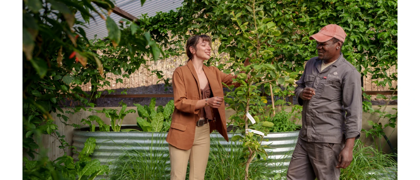 A staff member and female chat in a leafy garden under a blue sky