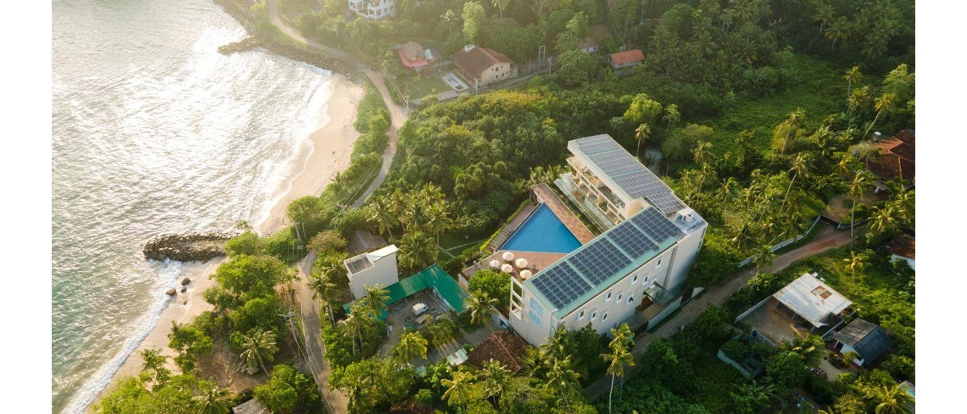 Resort topped with solar panels and surrounded by tropical greenery, with a triangle shaped pool and a beachfront location