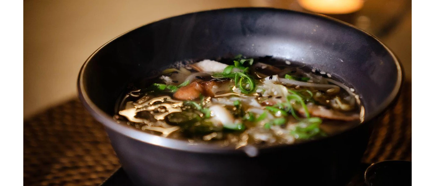 Black bowl of broth filled with green vegetables