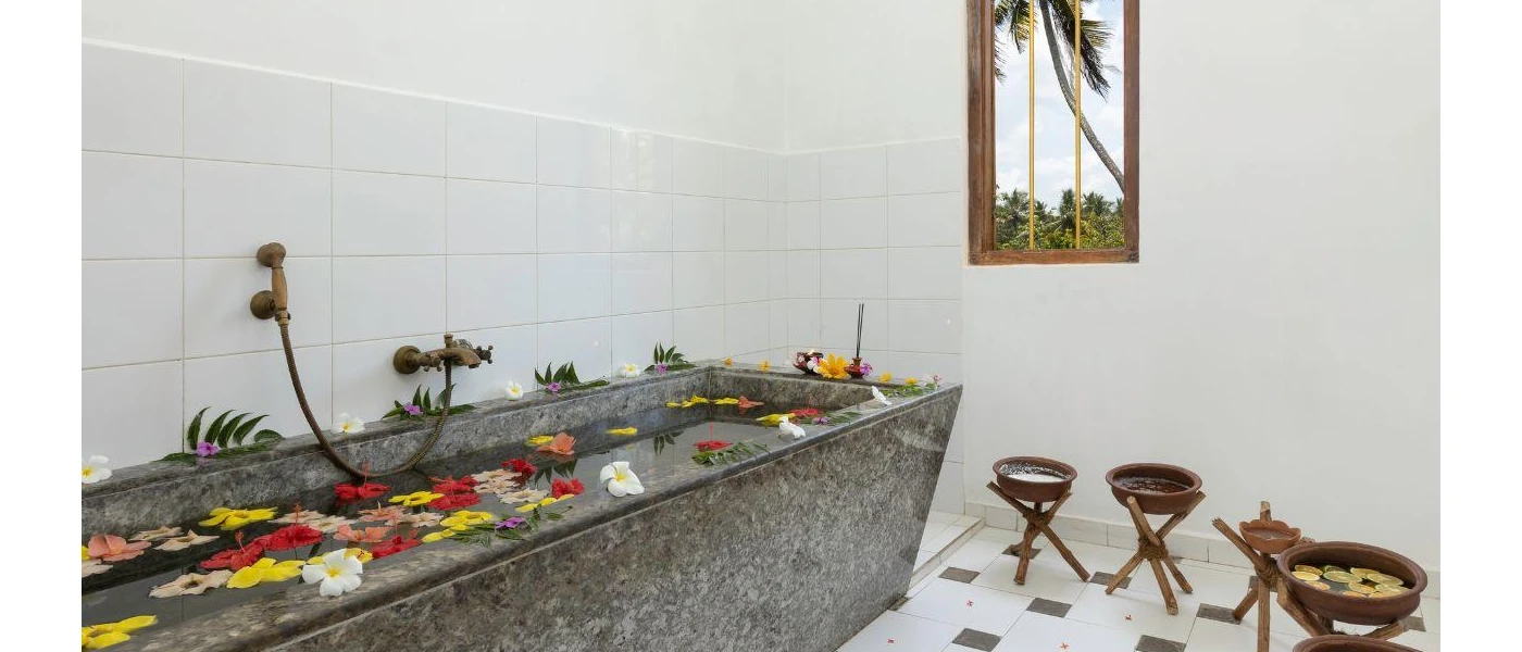 White room with a grey stone bath filled with water and flowers