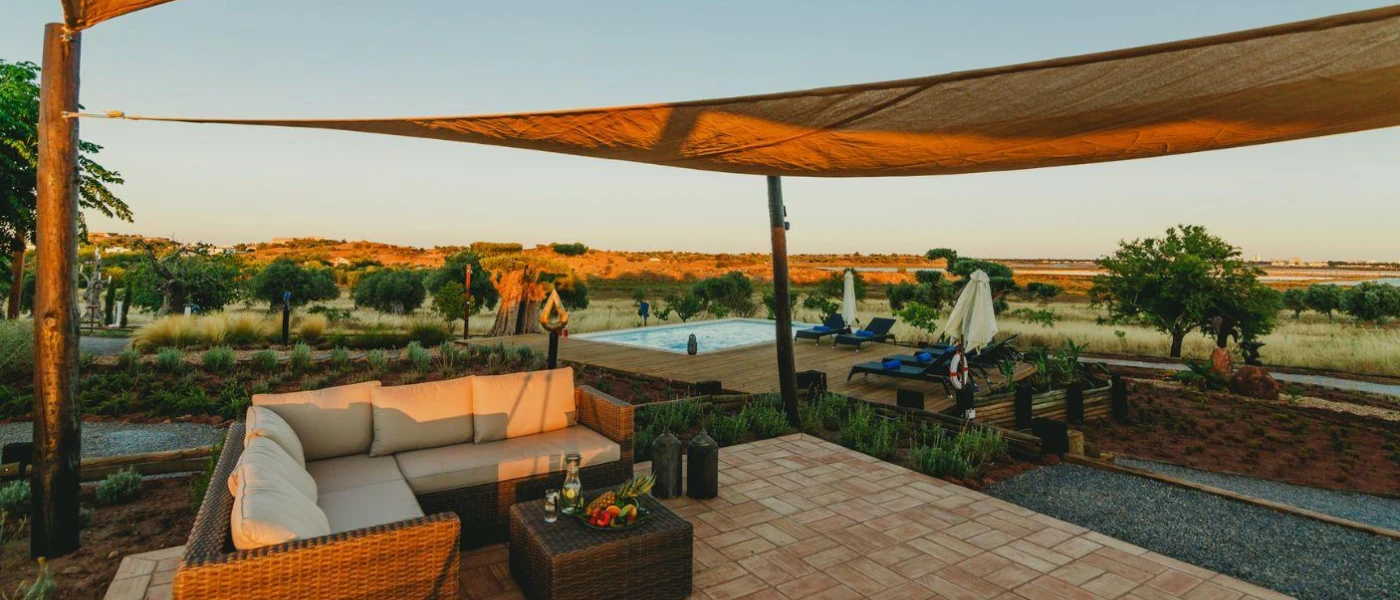 Open-air seating area with sofas and a roof covering, surrounded by greenery