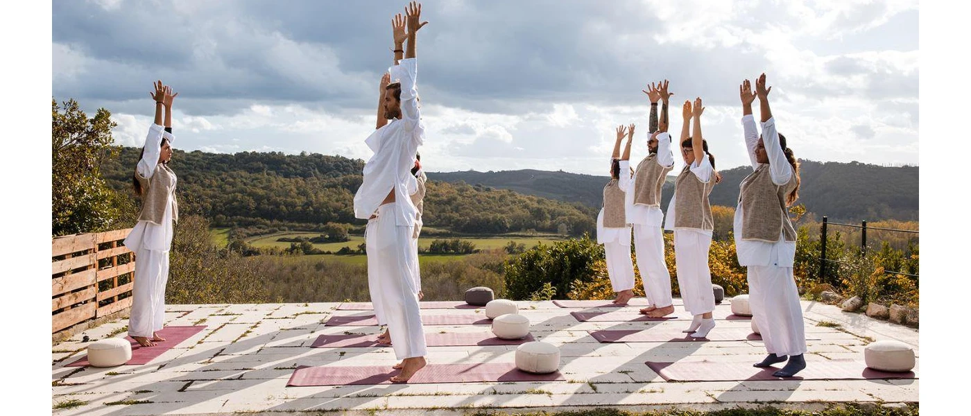 Group in white clothing on yoga mats stretch their arms up on a sunny outdoor terrace 