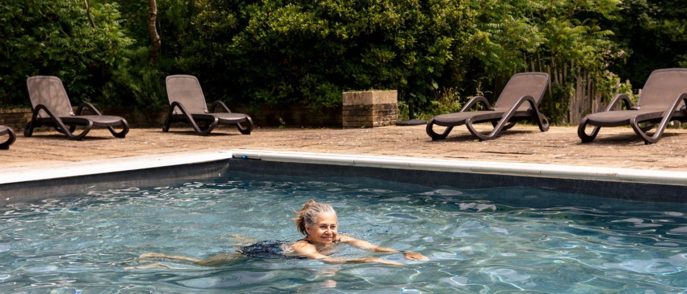 Woman swimming in an outdoor pool surrounded by wooden loungers and trees