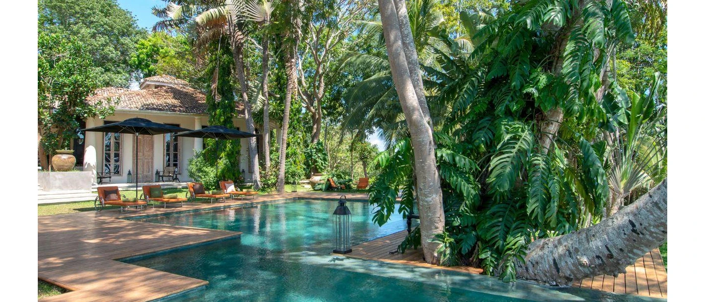 Tranquil pool area surrounded by greenery, black lanterns and orange loungers with navy umbrellas