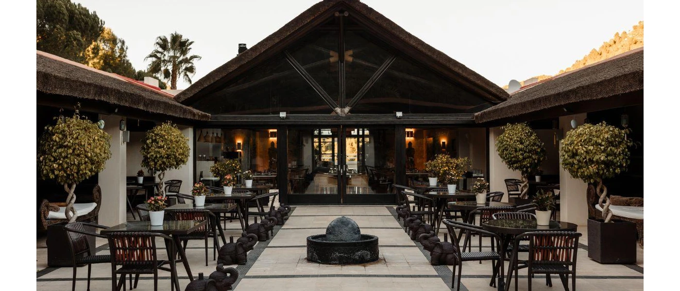 Courtyard with stone floors, a central black water fountain, black tables and chairs and surrounding potted trees
