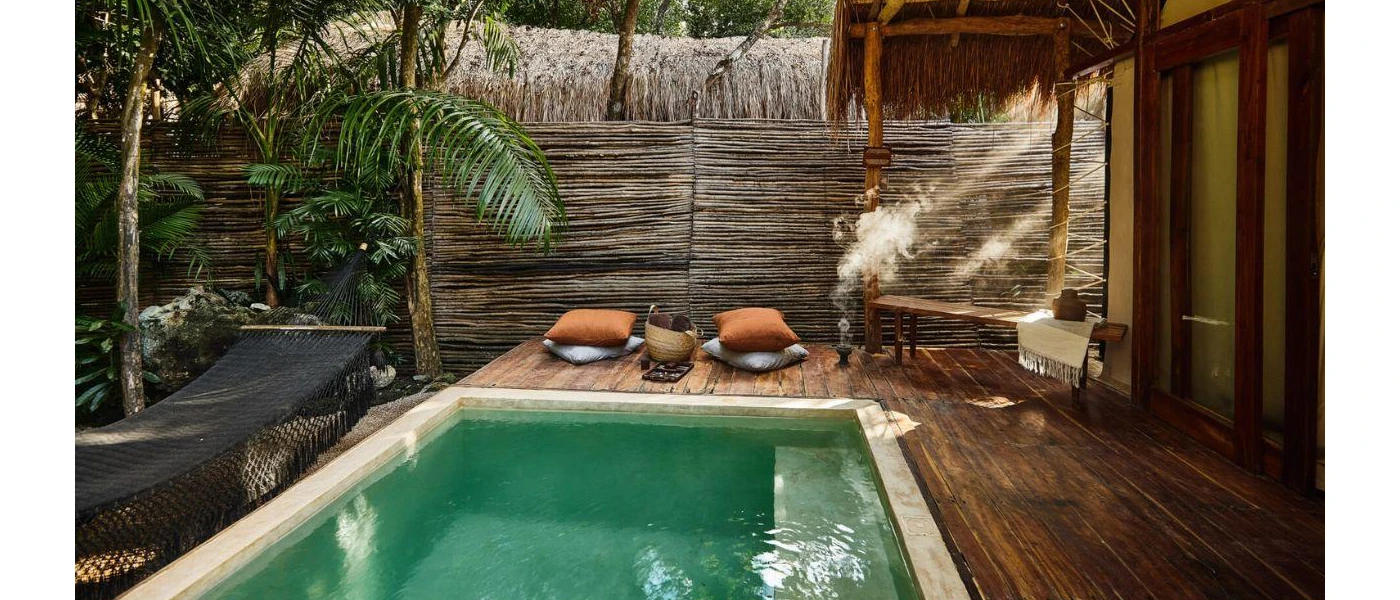 Palapa-roofed room with a wooden deck and private pool, fringed by tropical jungle greenery