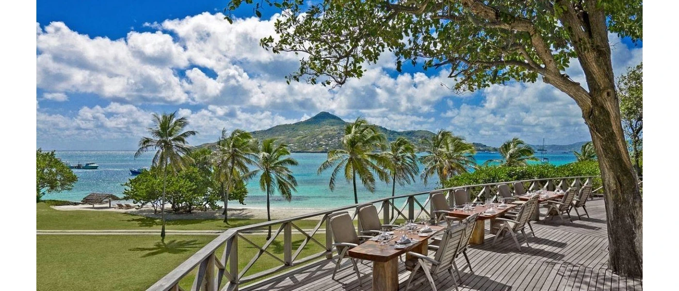 Outdoor restaurant terrace with wooden flooring, trees and a view of a lawn and ocean with mountains in the distance