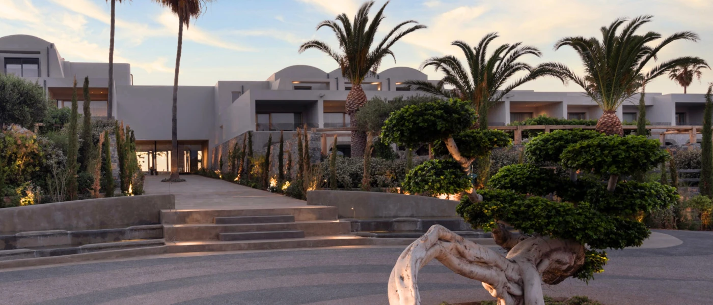 Low-rise cream resort surrounded by palms and shrubs, with steps into the entrance