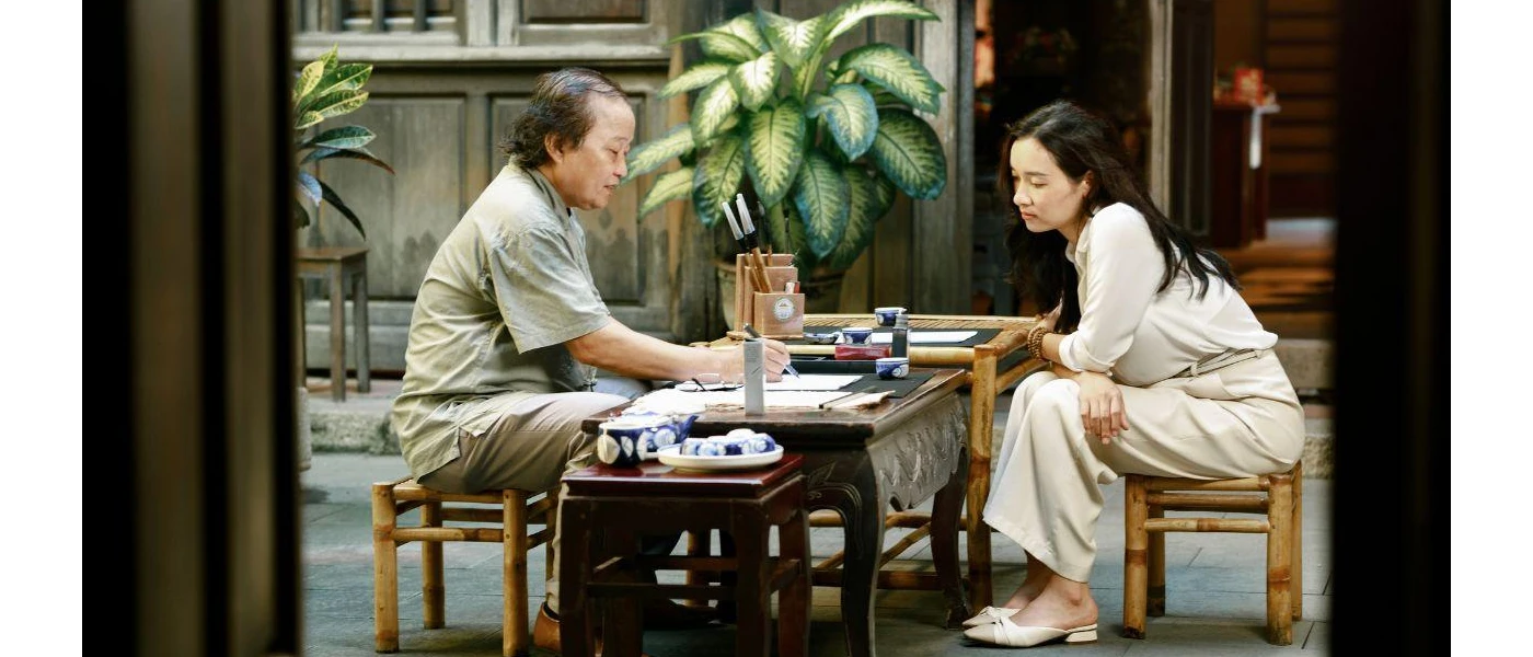 Woman sitting on a small wooden stall opposite a man, who is showcasing something to her by drawing or writing