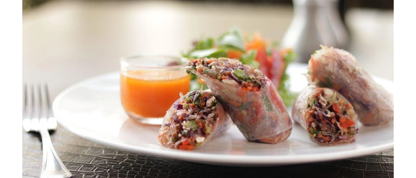 Sheer wraps packed with vegetables with an orange colour dip on a white plate