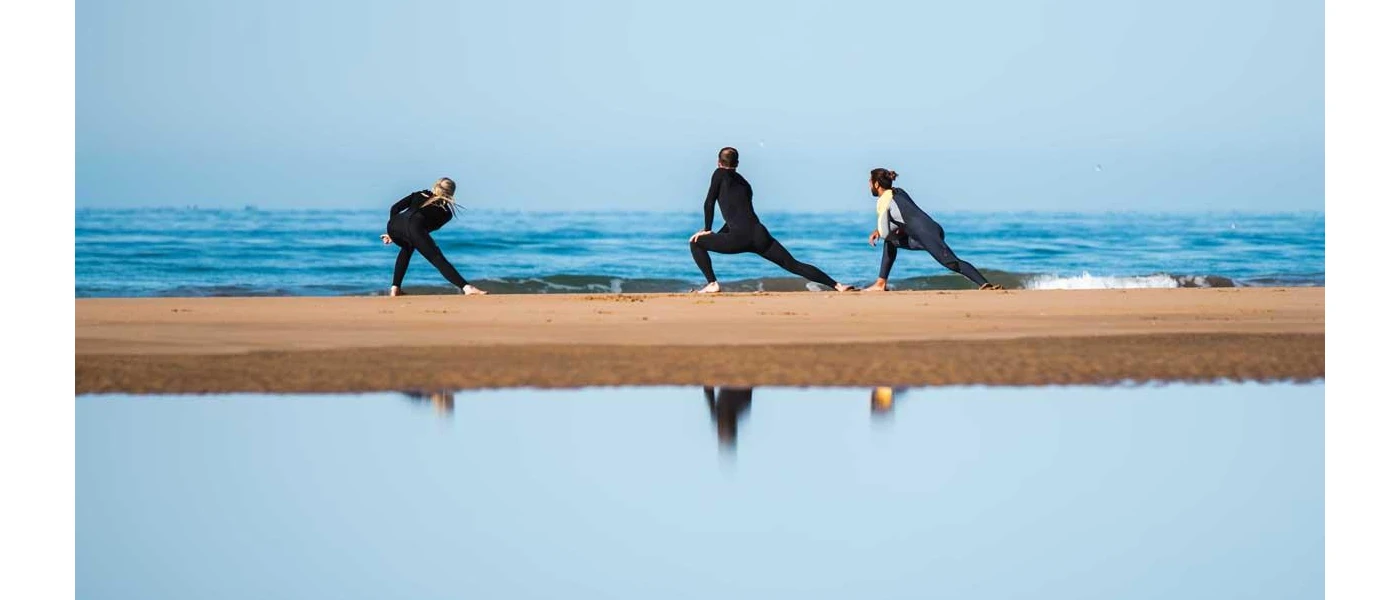Three people in active wear stretching on the shoreline 