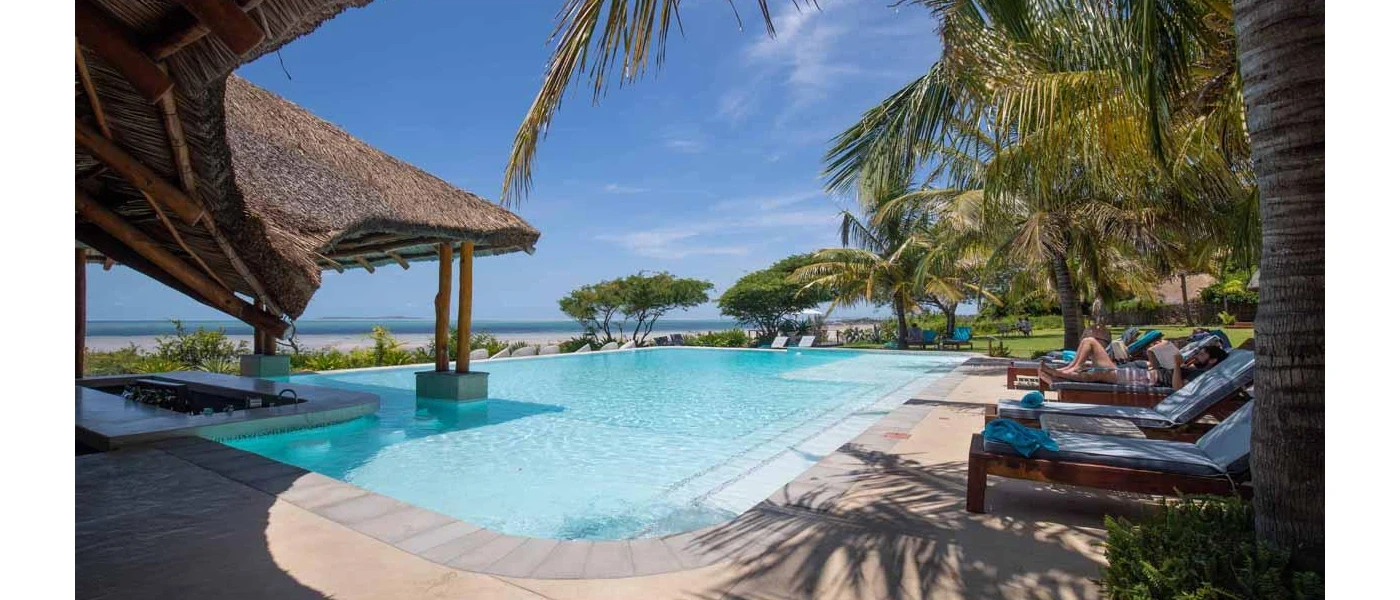 Infinity swimming pool with a thatched swim-up bar surrounded by loungers with blue towels and greenery