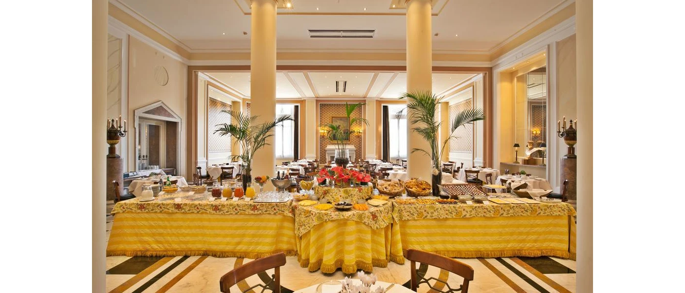 Airy restaurant with tall pillars and a long table with a gold tablecloth, laid up with breakfast options including jars of juices, bowls of cereal and baskets of pastries