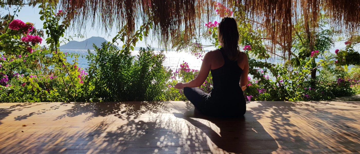 Woman in black active wear meditates among tropical gardens overlooking the sea and mountains