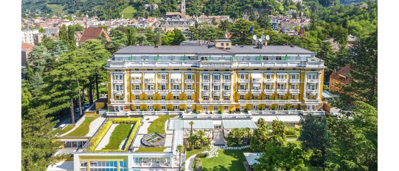 The grand exterior of Palace Merano, with its multiple storeys, gold-yellow walls and landscaped grounds