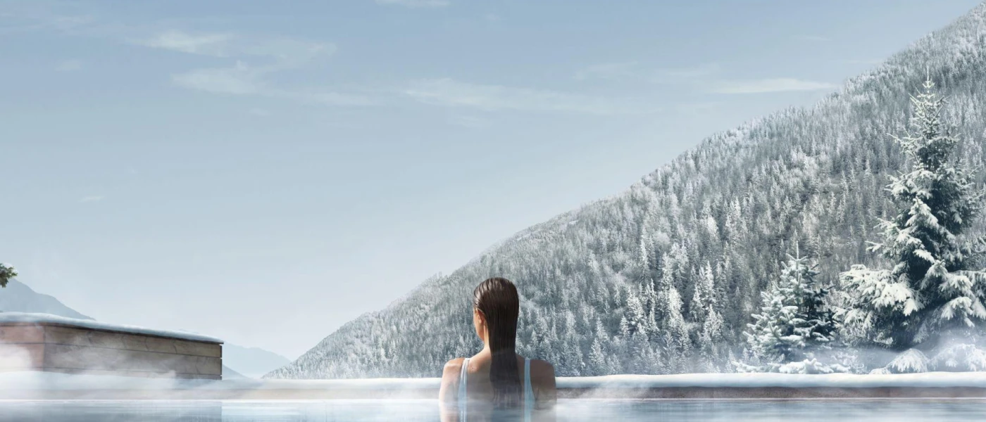 Woman at the edge of a heated pool, overlooking a snowy forested mountain