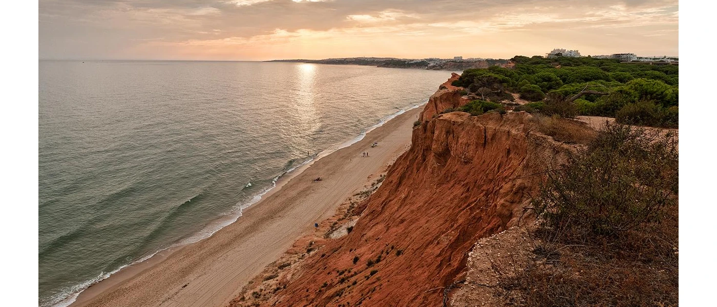 Golden sandy beach backed by red cliffs topped with greenery