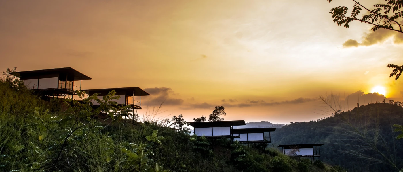 Standalone chalet-type buildings on stilts overlooking tropical greenery at sunset