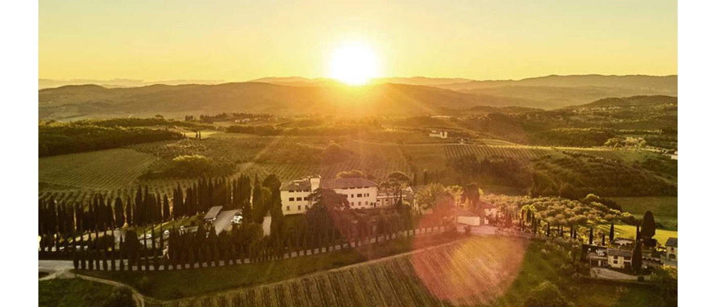 Aerial view of Catella del Nero's white buildings among lush vineyards and olive groves at sunset